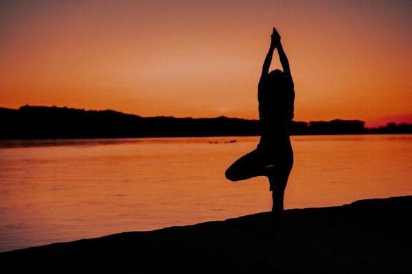Silhouette of a person in a powerful yoga warrior pose against a sunset.
